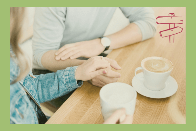 Eine Freuenhand liegt auf der Hand ihres Partners, gemeinsam statt einsam sitzen sie am Tisch bei einer Tasse Kaffee